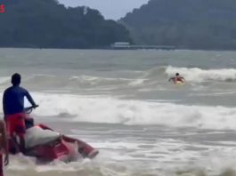 Livräddarna hann fram i tid – turist räddad ur strömmarna på Patong Beach Livräddare med jetski och gul räddningsbräda under en räddningsinsats i höga vågor på Patong Beach, Phuket.