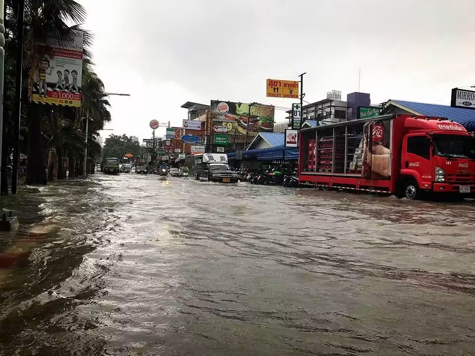 Flodvatten strömmar längs en väg i Pattaya med lastbilar och motorcyklar i vattnet