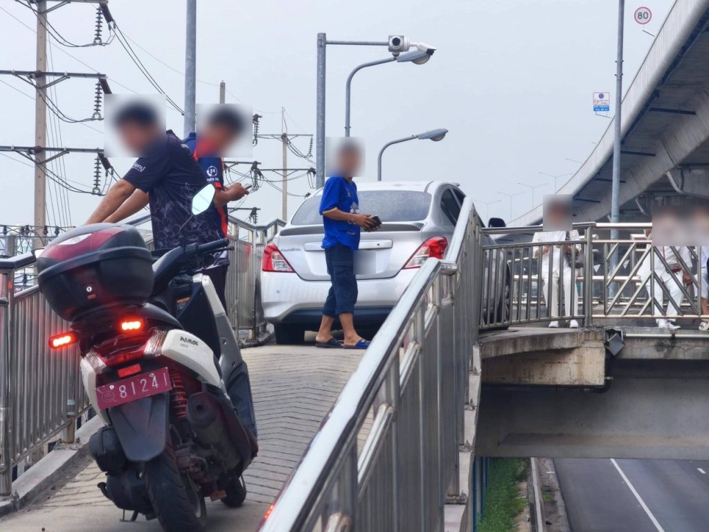Bil som star fast mellan racken pa en smal motorcykelramp medan folk star runt omkring