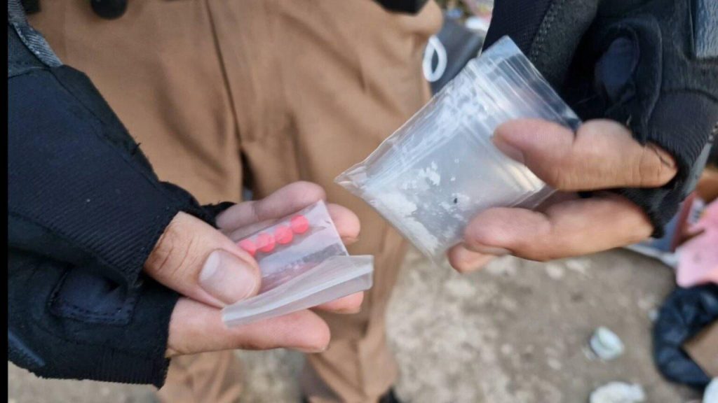 Polis haller upp tva plastpasar med roda tabletter och vitt pulver